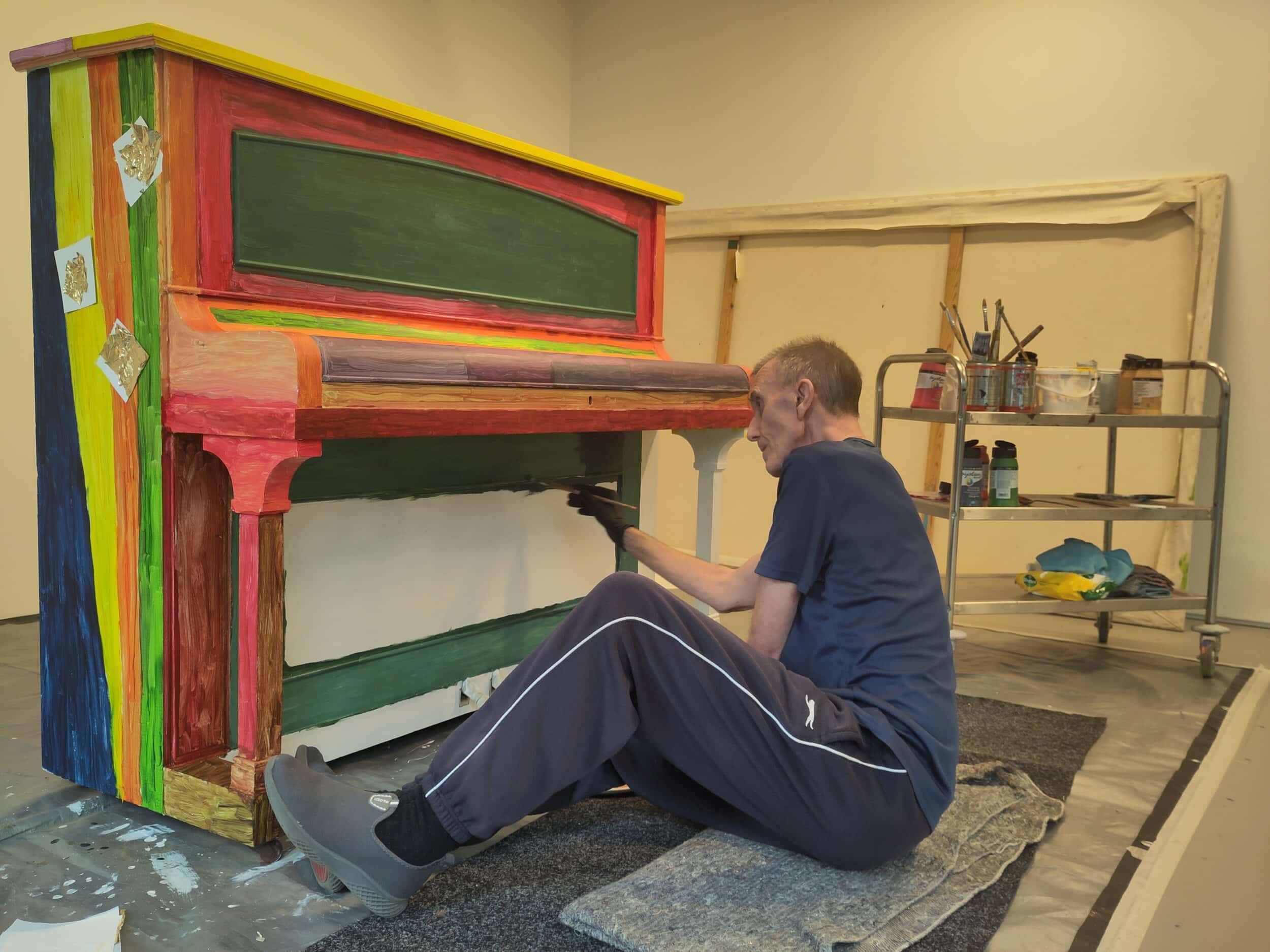 Mark decorates a piano in the studio. He is painting the piano in bright bold colours.
